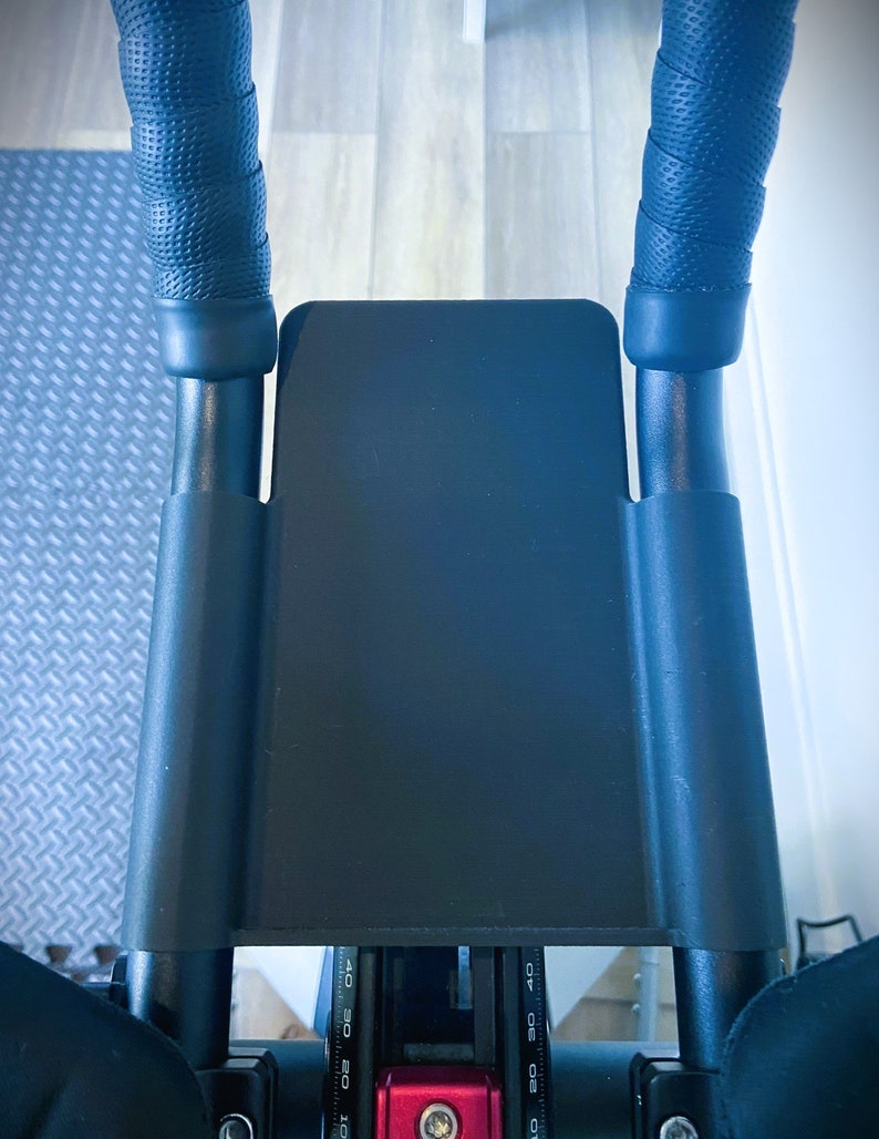 May include: Black exercise bike handlebars with black foam grips and a black metal frame. The handlebars have a black plastic cover with a red and black digital display that reads "10 20 30 40 50 60 70".