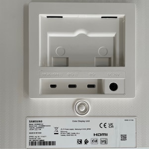 May include: White Samsung monitor back panel with ports for Micro HDMI, HDMI, Display Port, and DC 20V power. The panel also has a sticker with the model number, serial number, and other information. The sticker also includes the CE, UK, and CA certifications.