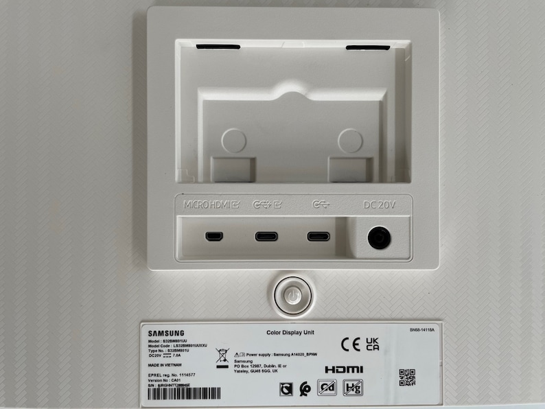 May include: White Samsung monitor back panel with ports for Micro HDMI, HDMI, Display Port, and DC 20V power. The panel also has a sticker with the model number, serial number, and other information. The sticker also includes the CE, UK, and CA certifications.