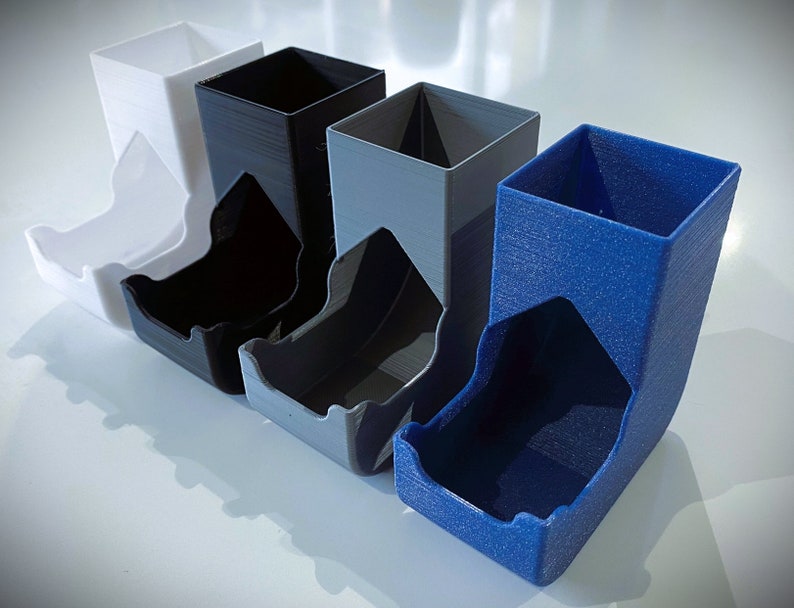 May include: Four dice towers in different colors: white, black, gray, and blue. The towers are made of plastic and have a textured surface.