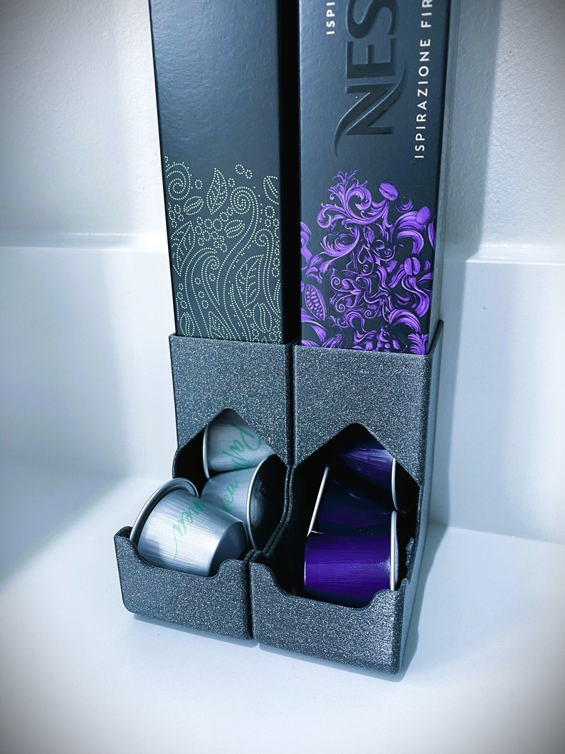 May include: A black and gray 3D printed coffee pod holder with two compartments. The holder is filled with silver and purple coffee pods. The holder is sitting on a white surface. The holder has the words "Nespresso" and "Ispirazione Firenze Artigianale" printed on the side.