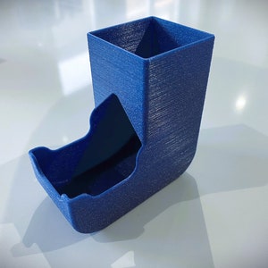 May include: A blue 3D printed dice tower with a square top and a curved bottom. The tower has a textured surface and a slot for dice to roll out.