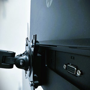 May include: A black computer monitor with an HP logo on the back. The monitor is attached to a black arm with a swivel joint. The monitor has a VGA port on the back.