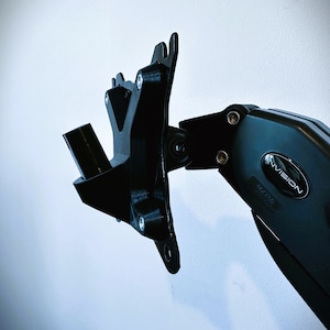 Puede incluir: Brazo de monitor negro con un soporte de pared en forma de V. El brazo está etiquetado como "INVISION MX100".