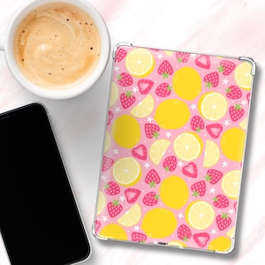 Op de afbeelding: Een doorzichtige tablethoes met een roze achtergrond met een patroon van gele citroenen, rode aardbeien en witte sterren. Een kopje koffie en een zwarte smartphone staan ook in de afbeelding.