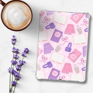 May include: A pink tablet case with a repeating pattern of books, scarves, headphones, bows, and notebooks. A cup of coffee and lavender sprigs are next to the tablet. The notebook has the text "Drawing Ideas".