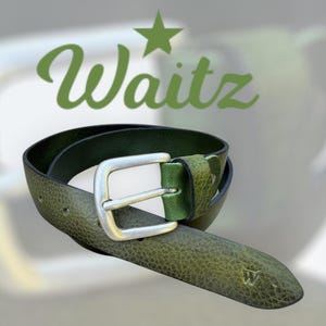 Op de afbeelding: Groene leren riem met een zilveren gesp. De riem heeft een getextureerd oppervlak en een kleine "W" in reliëf bij de punt. Het woord "Waitz" staat in groene letters boven de riem.