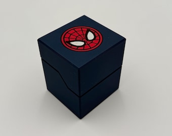 May include: A dark blue, square box with a hinged lid. The top of the box features a red and white Spider-Man logo. The box is likely for jewelry or a small gift.