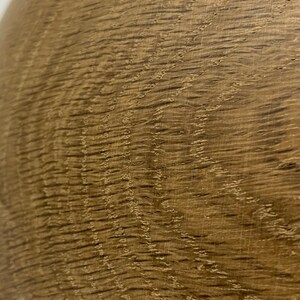 May include: Close-up of a section of wood grain. The wood has a warm, medium brown color with darker brown streaks and a textured surface. The grain pattern is visible, with wavy lines and small knots.