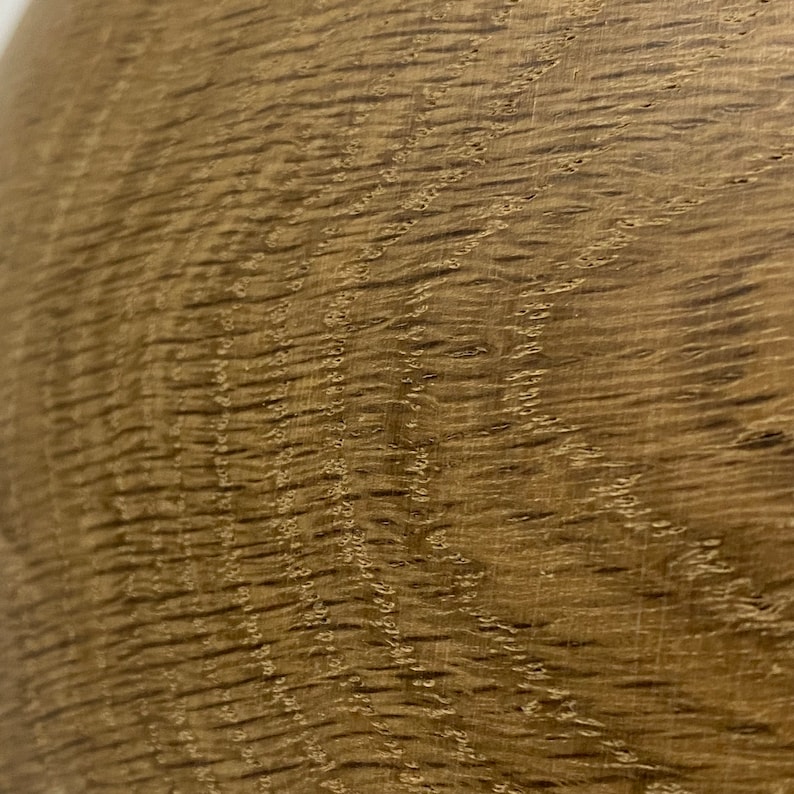 May include: Close-up of a section of wood grain. The wood has a warm, medium brown color with darker brown streaks and a textured surface. The grain pattern is visible, with wavy lines and small knots.