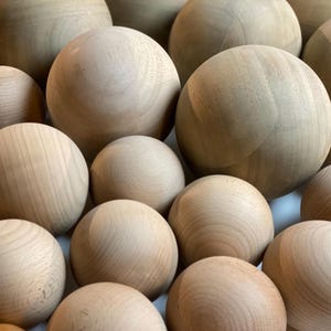 Puede incluir: Un grupo de esferas de madera de varios tama&ntilde;os, dispuestas en un patr&oacute;n aleatorio. Las esferas son de color marr&oacute;n claro y tienen un acabado liso y pulido.