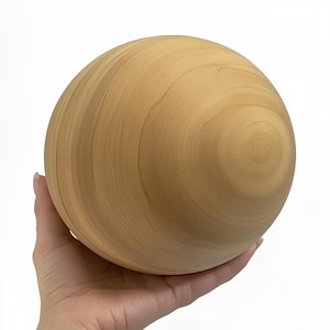 Puede incluir: Una esfera de madera lisa de color marrón claro. La esfera está siendo sostenida en una mano.