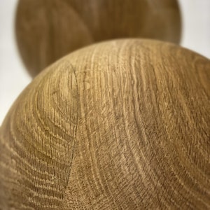 May include: Close-up of two wooden spheres with a natural wood grain pattern. The spheres are a light brown color and appear to be made of a hardwood. The wood grain is visible and adds texture to the spheres.
