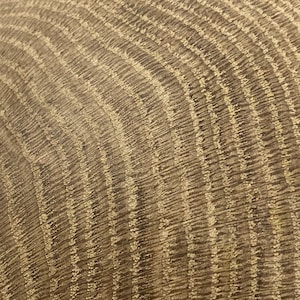 May include: Close-up of a textured, curved surface with a repeating pattern of vertical lines. The surface has a warm, neutral color palette with shades of brown and beige, creating a natural, organic aesthetic.