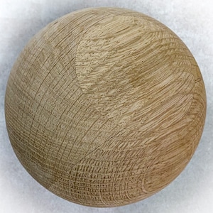 May include: A spherical wooden object with a light brown color and visible wood grain. The surface has a textured appearance with curved lines and small pores, suggesting it is made from a natural material.