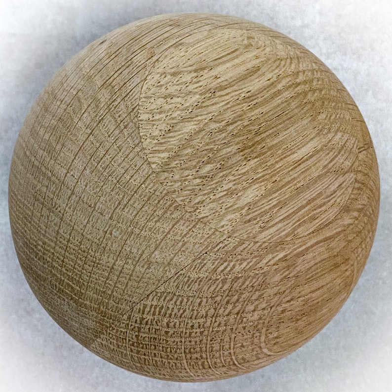 May include: A spherical wooden object with a light brown color and visible wood grain. The surface has a textured appearance with curved lines and small pores, suggesting it is made from a natural material.
