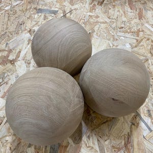 May include: Three wooden spheres with a natural wood grain pattern. The spheres are light brown and appear to be made of oak or a similar hardwood. The spheres are arranged in a triangular formation.