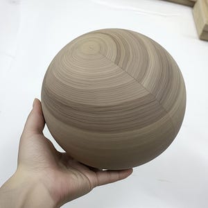 Puede incluir: Una esfera de madera lisa de color marrón claro con patrones de veta visibles.