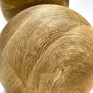 May include: Two spherical wooden decorative objects with a light brown color and a visible wood grain pattern. The objects are smooth and round, with a natural, organic aesthetic. The wood grain creates a textured surface.
