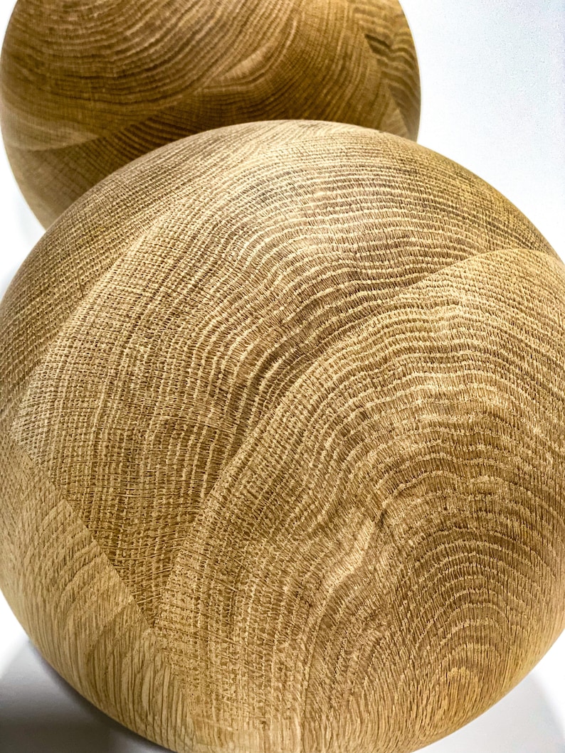May include: Two spherical wooden decorative objects with a light brown color and a visible wood grain pattern. The objects are smooth and round, with a natural, organic aesthetic. The wood grain creates a textured surface.
