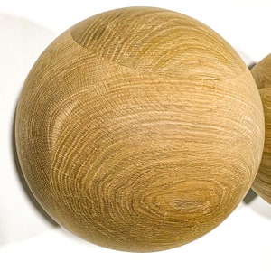 May include: Two wooden spheres with a natural wood grain pattern. The spheres are light brown and appear to be made of oak or a similar hardwood. The wood grain is visible and adds texture to the smooth, round shapes.