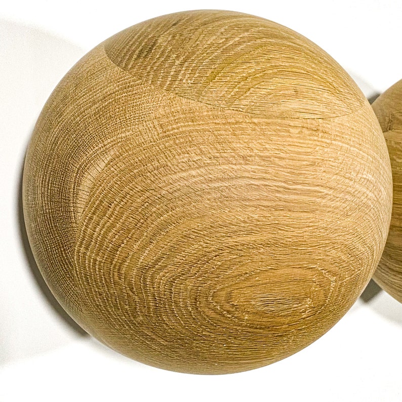 May include: Two wooden spheres with a natural wood grain pattern. The spheres are light brown and appear to be made of oak or a similar hardwood. The wood grain is visible and adds texture to the smooth, round shapes.