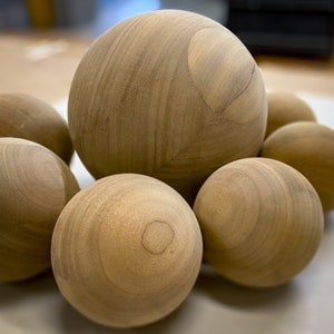 Puede incluir: Un grupo de seis esferas de madera lisas en varios tonos de marr&oacute;n. Las esferas est&aacute;n dispuestas en un racimo, con la esfera m&aacute;s grande en el centro.