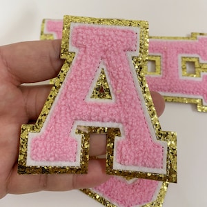 May include: Pink felt letter A with a gold glitter outline. The letter is approximately 10 cm tall and is ideal for crafting projects.