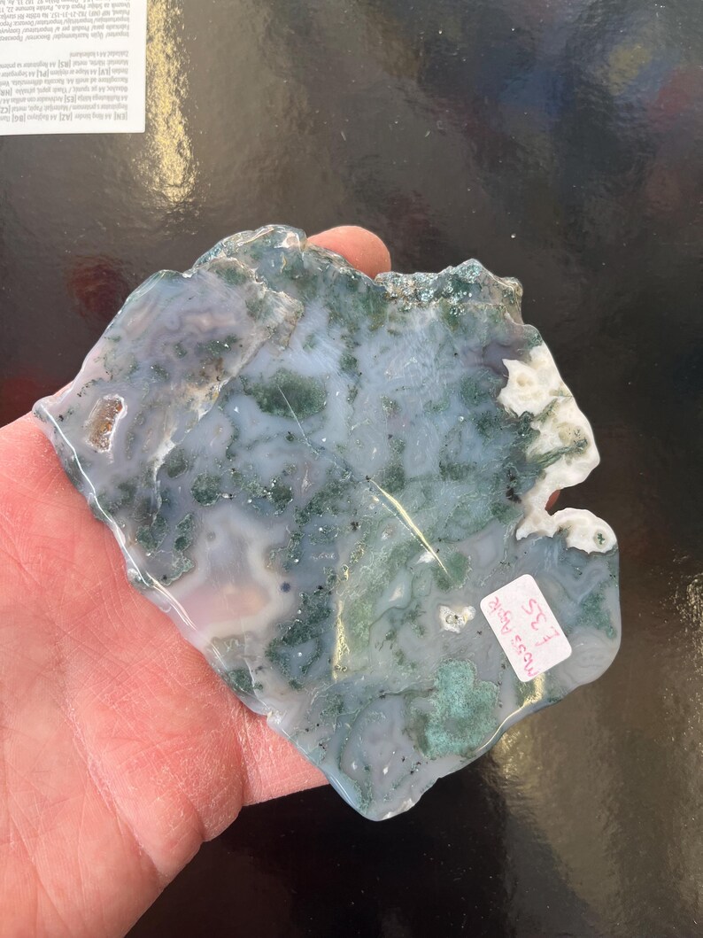 Puede incluir: Una losa de &aacute;gata verde y blanca con una forma natural irregular. La losa tiene una superficie lisa y pulida y presenta una variedad de patrones verdes y blancos. La losa est&aacute; etiquetada como "Moss Agate #32".