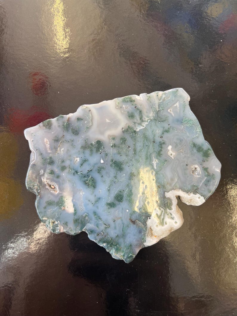 Puede incluir: Una rebanada de &aacute;gata verde y blanca con un patr&oacute;n &uacute;nico de remolinos y l&iacute;neas. La &aacute;gata es una piedra natural y tiene una superficie lisa y pulida.