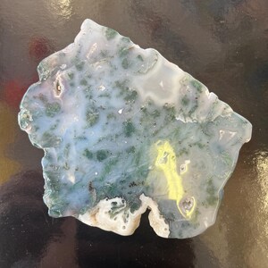 Puede incluir: Una rebanada de &aacute;gata verde y blanca con una forma &uacute;nica e irregular. La &aacute;gata es transl&uacute;cida y presenta una variedad de patrones y texturas.