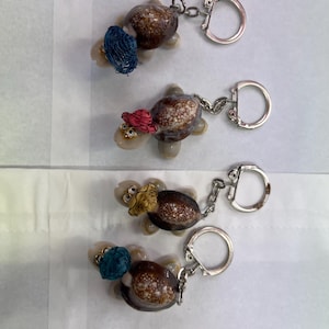 May include: Four turtle keyrings made from seashells. Each turtle has a different coloured hat and a silver key ring.