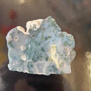 Puede incluir: Una rebanada de &aacute;gata verde y blanca con una forma natural irregular. La &aacute;gata tiene un patr&oacute;n de remolino de verde y blanco, con algunas &aacute;reas de blanco claro.