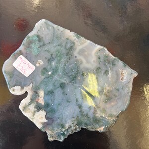 Puede incluir: Una losa de &aacute;gata verde, blanca y marr&oacute;n con una forma natural irregular. La losa mide aproximadamente 25 cm de largo y 18 cm de ancho. La &aacute;gata tiene una variedad de patrones y colores, incluyendo verde, blanco, marr&oacute;n y negro. La losa est&aacute; sobre una superficie negra. Moss Agate &pound;35