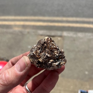 Puede incluir: Primer plano de una roca marrón oscura y dorada con una superficie rugosa y texturizada. La roca tiene una estructura cristalina y parece ser un mineral natural.