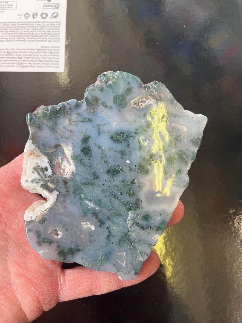 Puede incluir: Una rebanada de &aacute;gata verde y blanca con un patr&oacute;n &uacute;nico. La &aacute;gata tiene una superficie lisa y pulida y es una piedra natural.