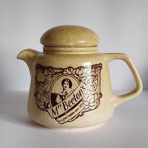May include: A beige ceramic teapot with a brown floral design and the text "Mrs. Beeton's In a great tradition since 1861".