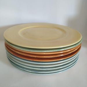Può includere: Un set di dieci piatti da cena in ceramica di diverse tonalità di blu, verde e arancio. Il piatto superiore è di colore giallo pallido con un delicato motivo a spirale.