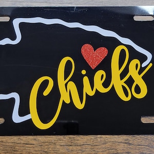 May include: Black license plate with a white outline of the state of Missouri and the word "Chiefs" in yellow with a red heart above it.