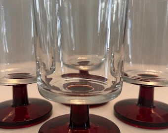 Könnte beinhalten: Set aus vier klaren Trinkgläsern aus Glas mit roten Füßen. Die Gläser haben ein schlichtes Design und sind perfekt für den täglichen Gebrauch.