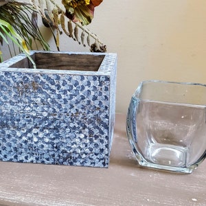 May include: A square wooden planter with a blue and white speckled paint finish, and a clear glass square vase with rounded edges.