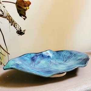 May include: A blue and green ceramic serving dish with a wavy edge. The dish is shaped like a leaf and has a subtle glaze.