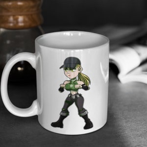 May include: White ceramic mug featuring a cartoon illustration of a female character in a green and black outfit, wearing a black cap. The character is holding a weapon in each hand.