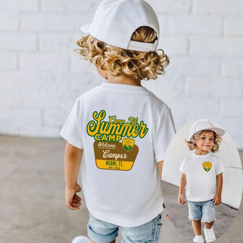 May include: A white t-shirt with a graphic that says "Camp Titi Summer Camp Camper Miami, FL Est. 2020" in green, yellow, and brown. The shirt is worn by a young child wearing a white baseball cap and denim shorts.