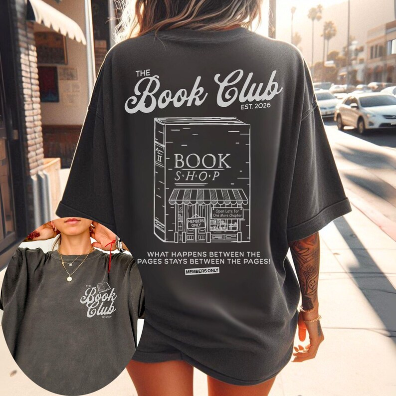 K&ouml;nnte beinhalten: Dunkelgraues T-Shirt mit wei&szlig;er Grafik eines Buchladens und dem Text "The Book Club EST. 2026." Das Shirt zeigt auch den Text "Was zwischen den Seiten passiert, bleibt zwischen den Seiten!"