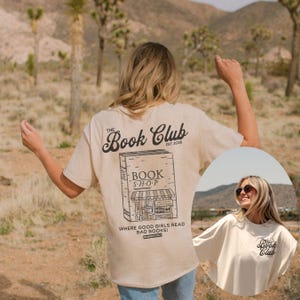 K&ouml;nnte beinhalten: Beiges T-Shirt mit schwarzer Buchladen-Grafik und dem Text "The Book Club" und "Where good girls read bad books!". Das Shirt hat eine lockere Passform.