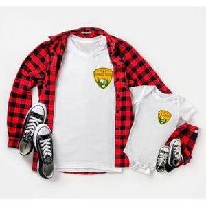 May include: A white t-shirt with a "Made in USA Director" patch, a red and black plaid shirt, a white baby onesie with a "Camper" patch, and matching plaid shorts. Black canvas sneakers are also included.