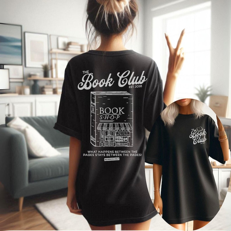 K&ouml;nnte beinhalten: Schwarzes T-Shirt mit wei&szlig;em Text und Illustration. Der Text lautet "The Book Club" &uuml;ber einer Zeichnung eines Buchladens mit den Worten "BOOK SHOP" und "EST. 2026". Darunter steht der Text "WHAT HAPPENS BETWEEN THE PAGES STAYS BETWEEN THE PAGES!"