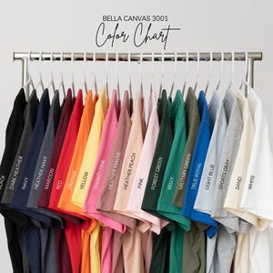 May include: A color chart of Bella Canvas 3001 t-shirts, displayed on a metal rack. The shirts are in various colors, including black, navy, red, yellow, pink, green, and blue. The text "Color Chart" is at the top.