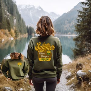 Puede incluir: Sudadera verde oliva con dise&ntilde;o "Smiths Summer Camp" en amarillo y marr&oacute;n. El dise&ntilde;o incluye las palabras "Welcome Camper Logan, Utah" y un peque&ntilde;o emblema. La sudadera se lleva al aire libre.